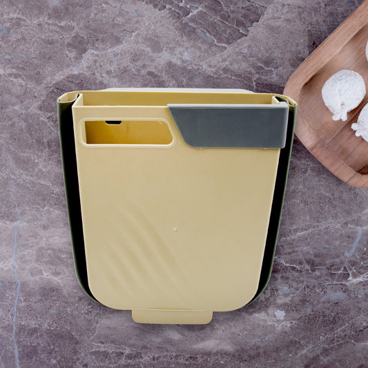 A white foldable hanging trash can attached to a kitchen cabinet door, collecting waste.